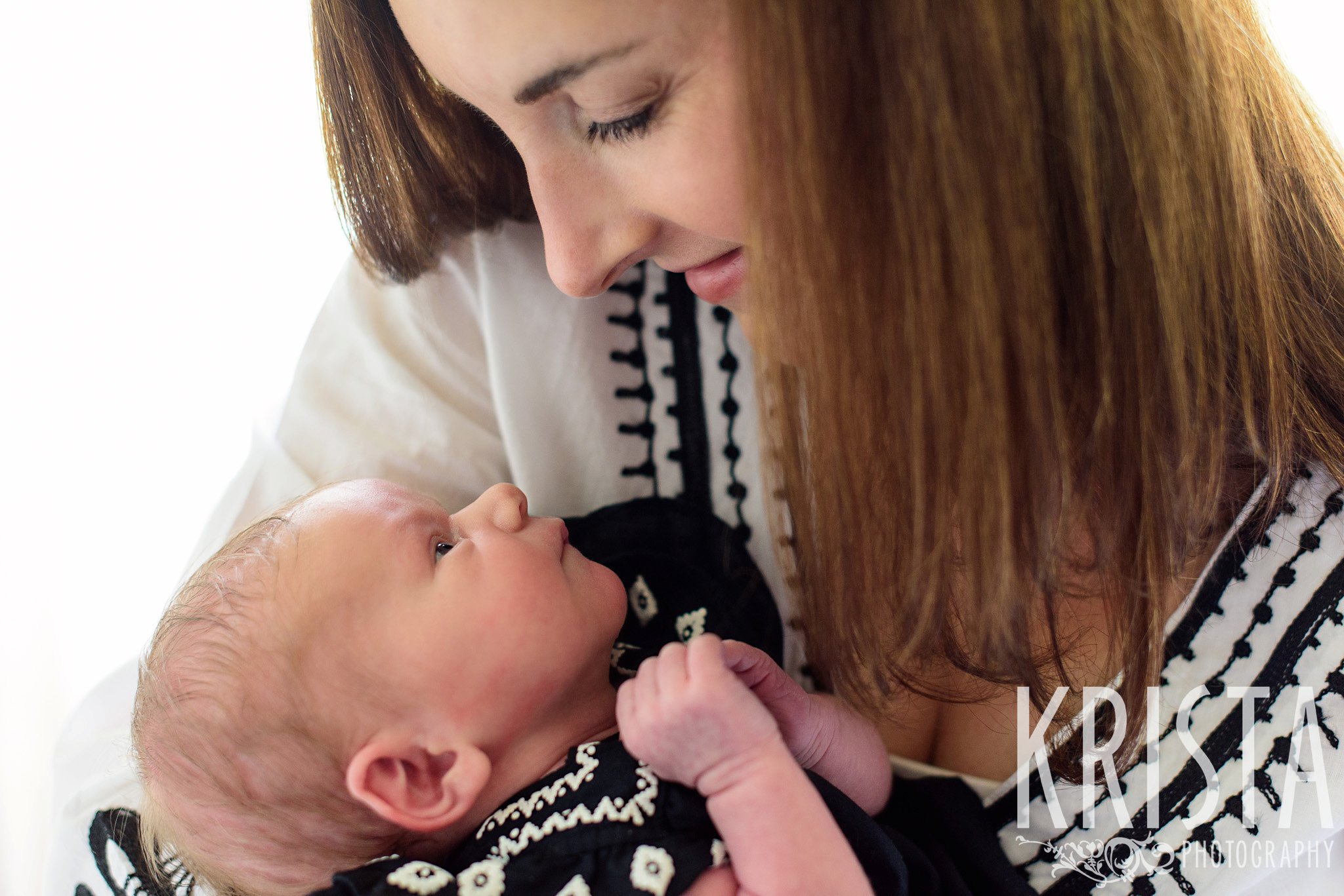 mother looking at newborn baby girl during lifestyle family portrait session in family home