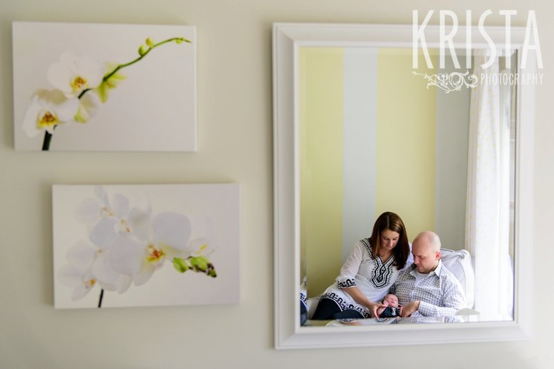 mother, father and newborn baby girl reflected in mirror of yellow, white and gray nursery during lifestyle family portrait session at family home