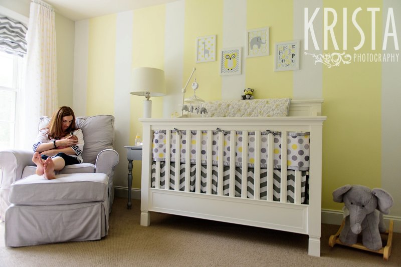 mother nursing newborn baby girl on white arm chair in yellow white and gray nursery during lifestyle family portrait session at family home