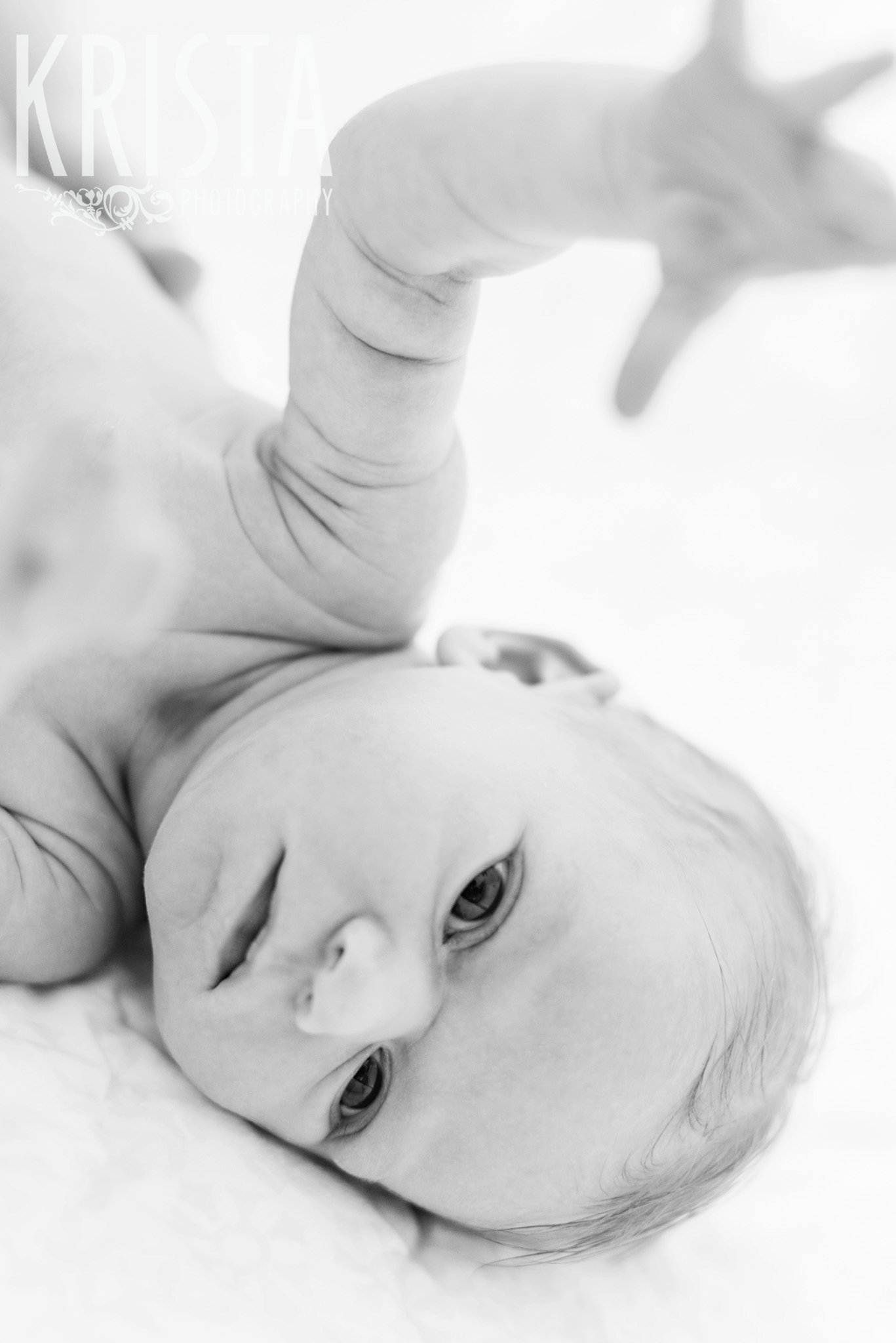 black and white image of newborn baby girl with arm and hand up in air during lifestyle family portrait session at family home