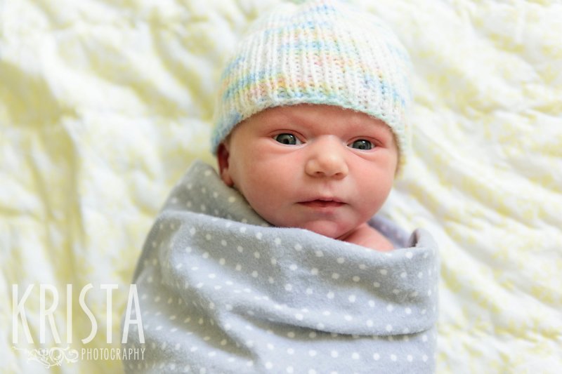 newborn baby girl swaddled and with knitted hat during lifestyle family portrait session at home