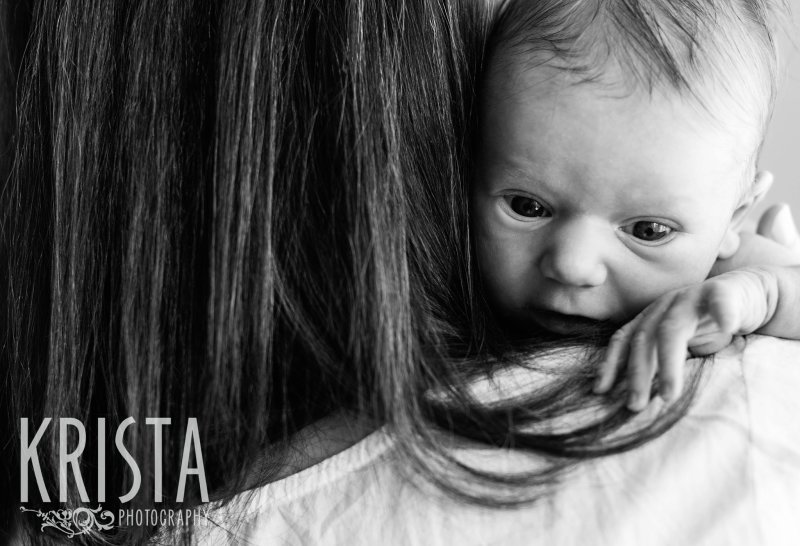 black and white image of newborn baby girl on mother's shoulder during lifestyle family portrait session at home