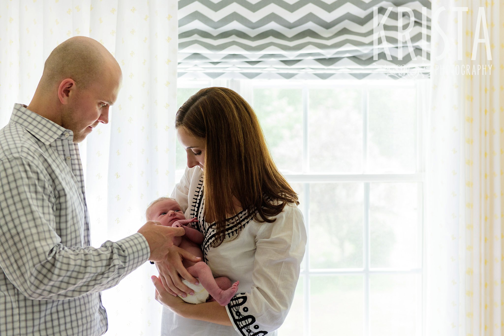 newborn baby girl with parents in her yellow white and gray nursery during lifestyle family session