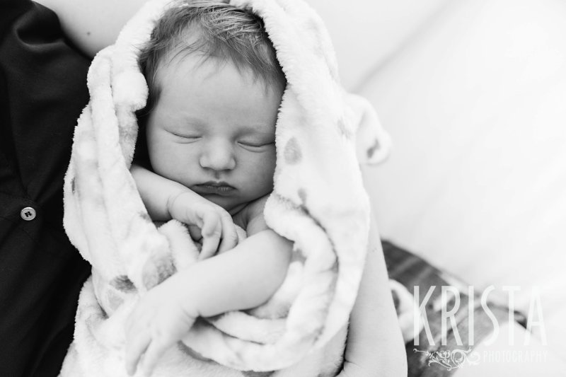 black and white newborn baby girl wrapped in loose blanket sleeping with eyes shut during lifestyle portrait session at home