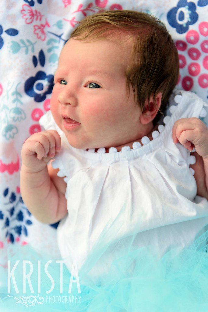 newborn baby girl in aqua tutu on pink blue and aqua blanket eyes open smiling during lifestyle family portrait session at home
