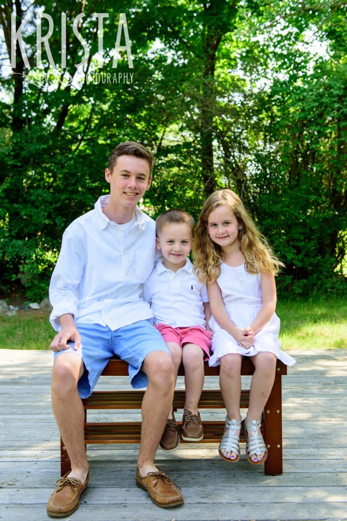 two brothers and a sister on a wood bench in the spring in New England for mini portrait session