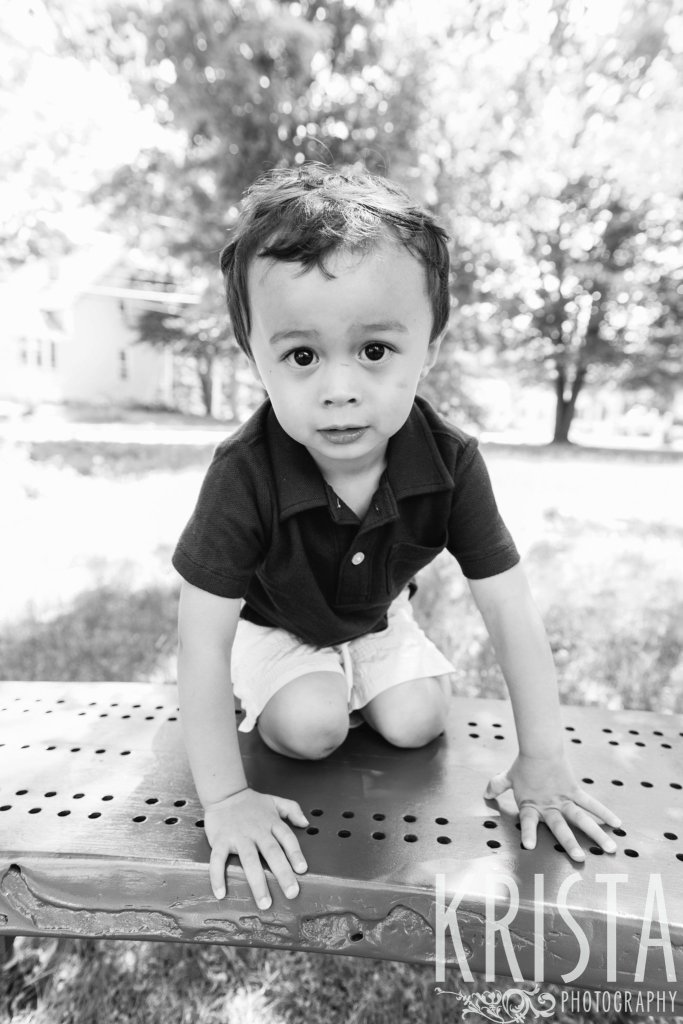 toddler boy in collared shirt climbing on bench during springtime mini portrait sessions in New England