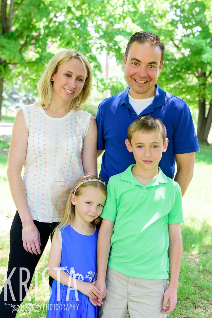 family in blues and greens standing among green trees during springtime mini portrait sessions in New England