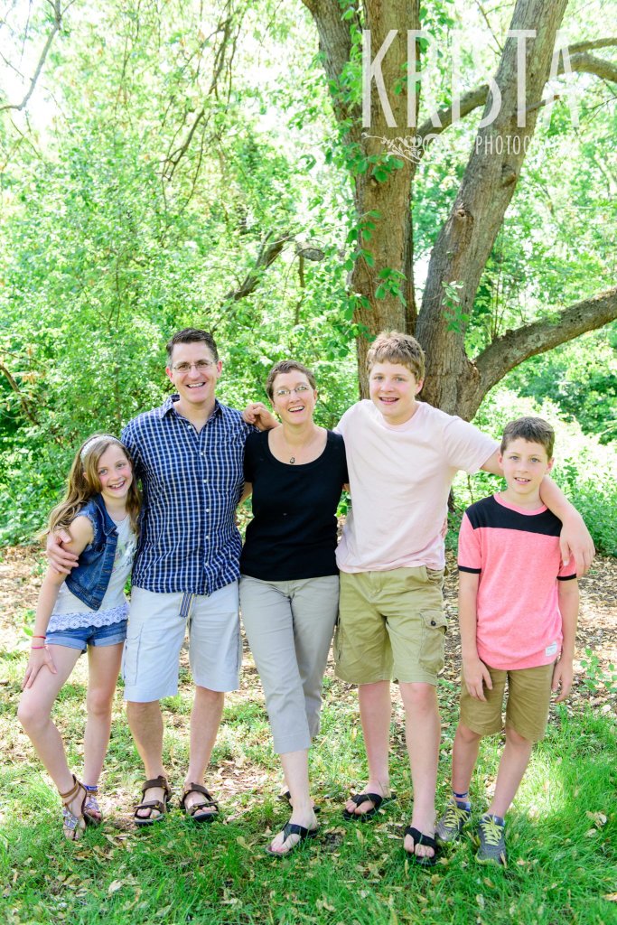 family of five with arms around one another among green trees during springtime mini portrait session in New England