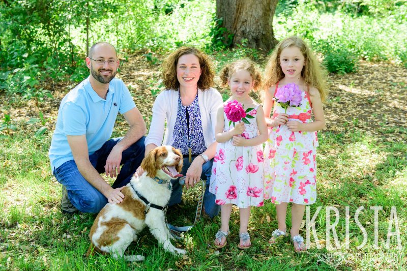 adorable family with two little sisters and dog among green trees during spring mini portrait session