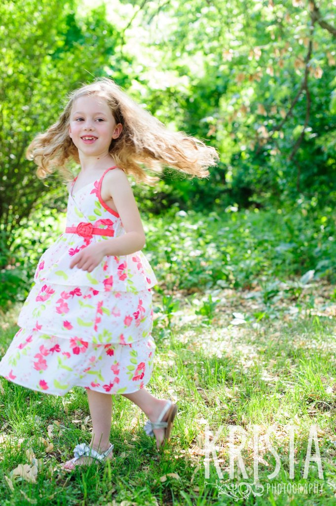 twirling little girl in floral dress among green trees during spring mini portrait session