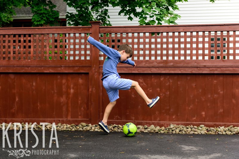boy kicking soccer ball on driveway during lifestyle family portrait session at home