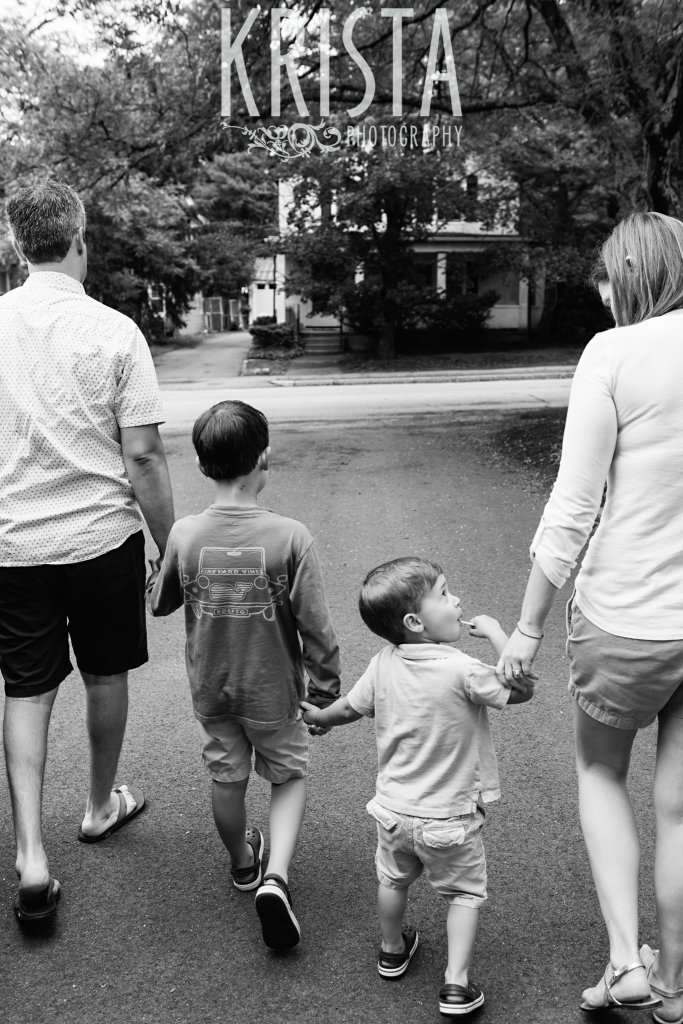 black and white of mother father and two sons walking hand in hand from behind