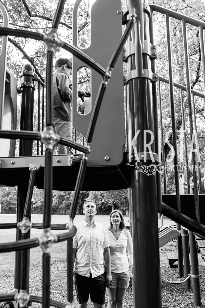 black and white of parents watching kids from below playing on structure at playground
