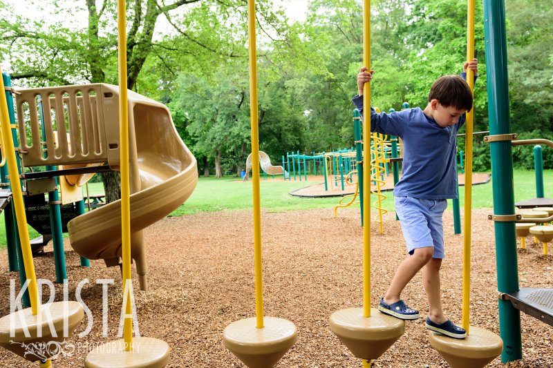 young boy in blue crossing a play structure on playground