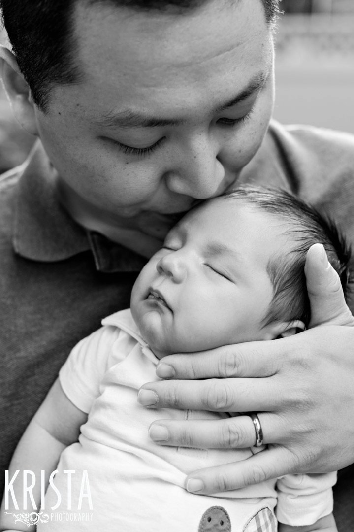 black and white image of father kissing newborn baby boy's forehead during outdoor lifestyle family portrait session