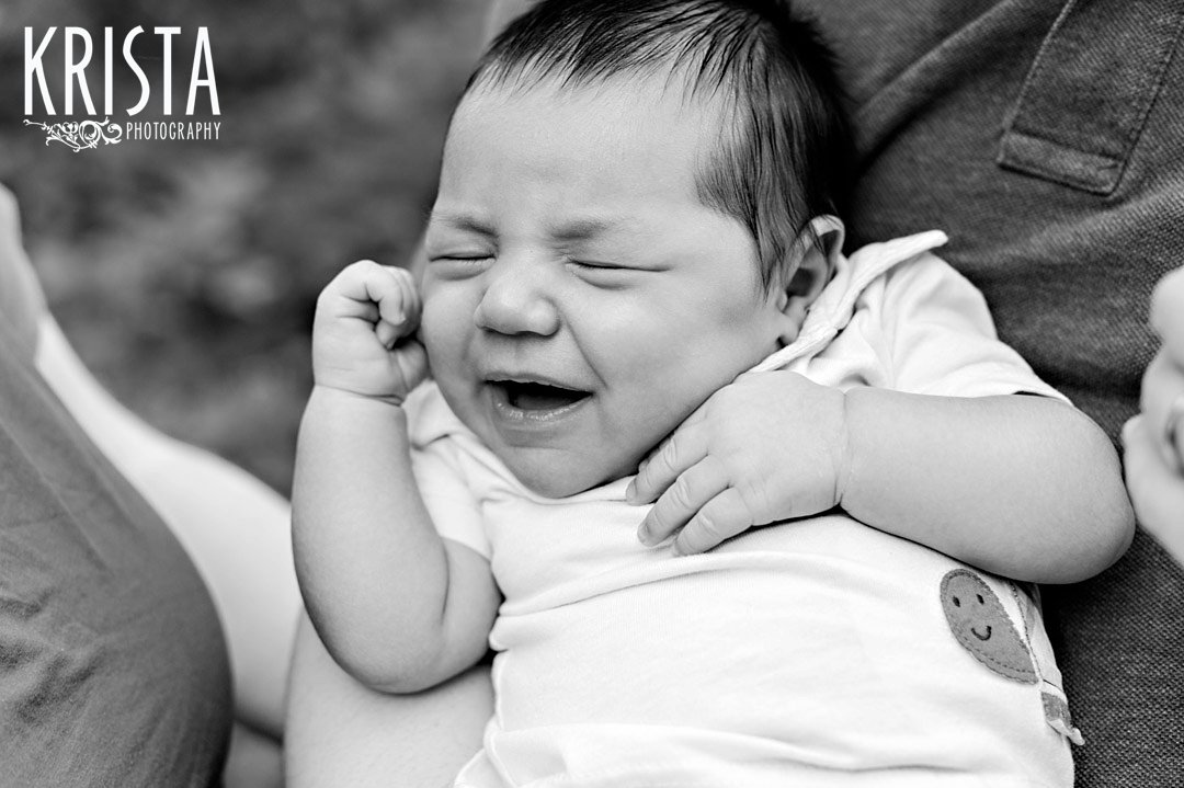 black and white image of newborn baby boy laughing or smiling while he sleeps during outdoor lifestyle portrait session at home