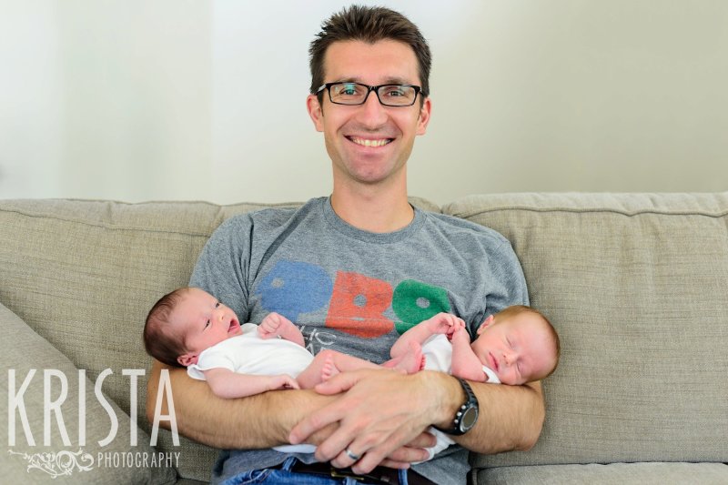 father in PBS shirt holding newborn baby twins on couch at home