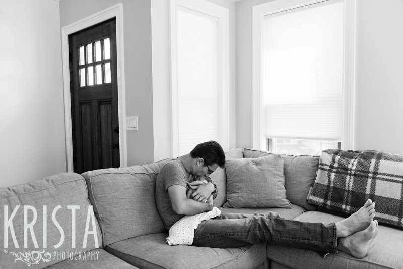 black and white of father cuddling newborn baby twin in home during portrait session