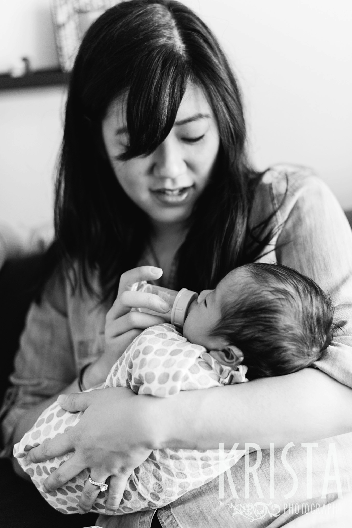 black and white image of mother feeding newborn baby boy a bottle during family portrait session in their home