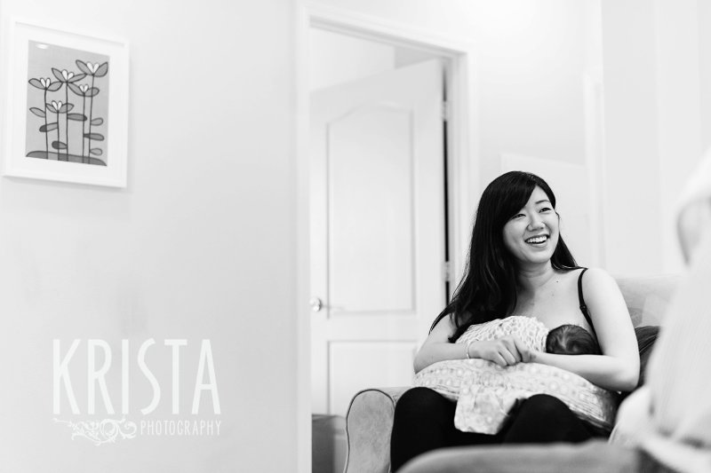 black and white image of mother feeding newborn baby boy during family portrait session in their home