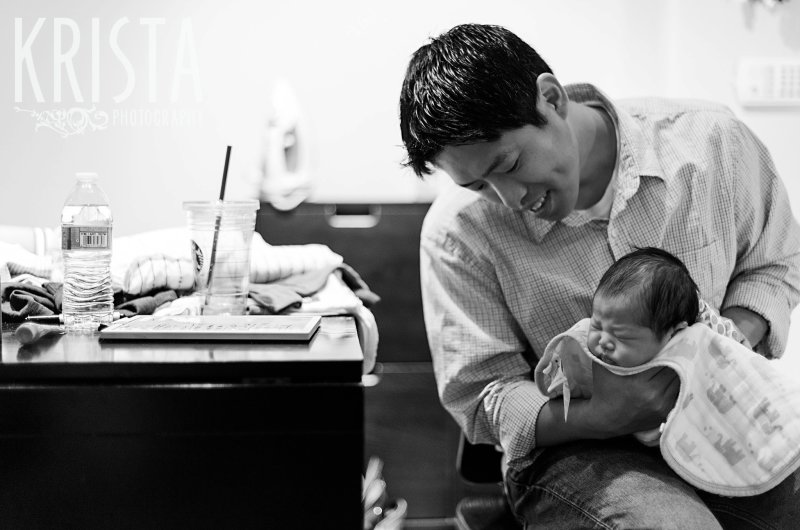 black and white image of father burping newborn baby boy during family portrait session in their home