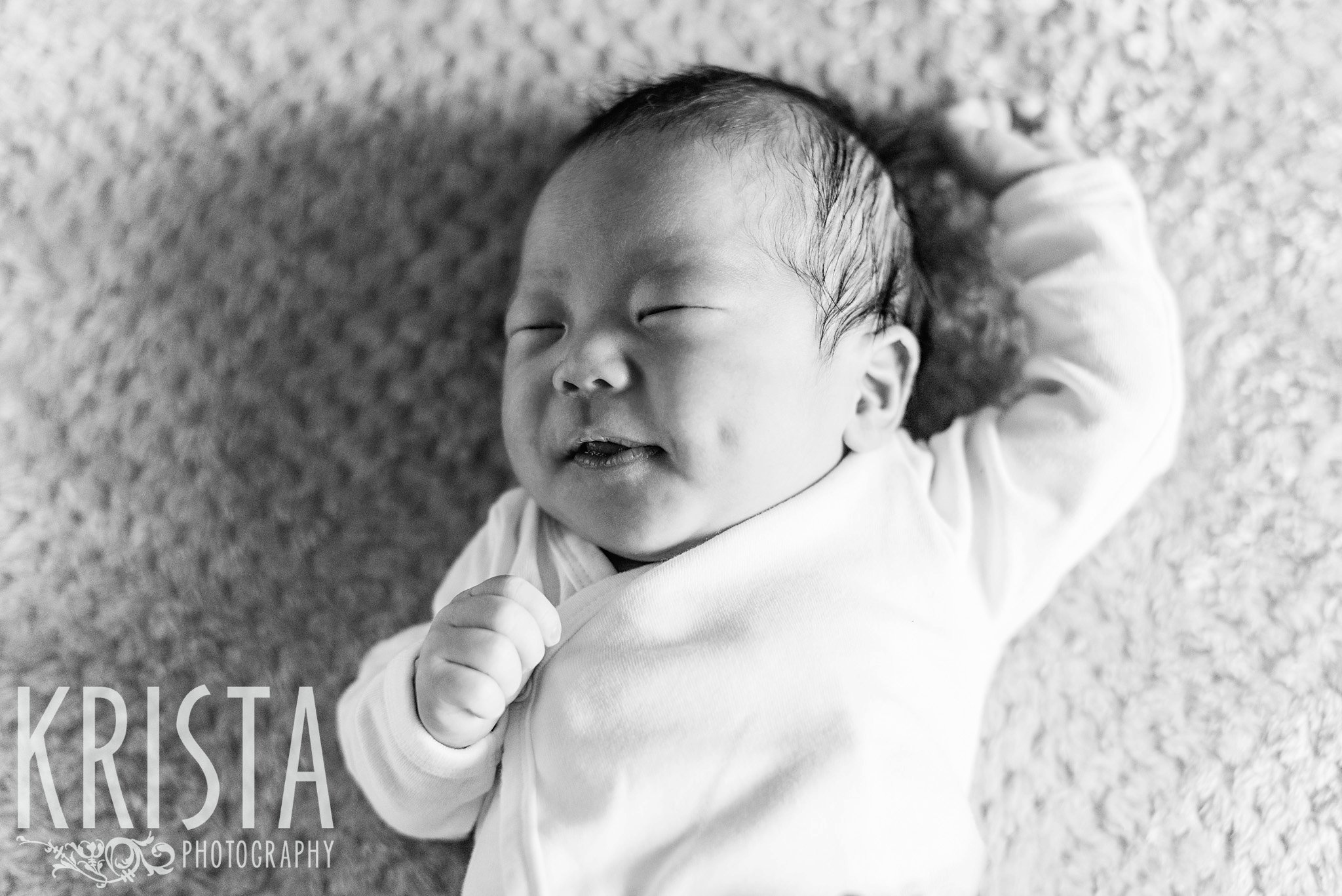 black and white image of newborn baby boy grinning in his sleep with dimples flashing