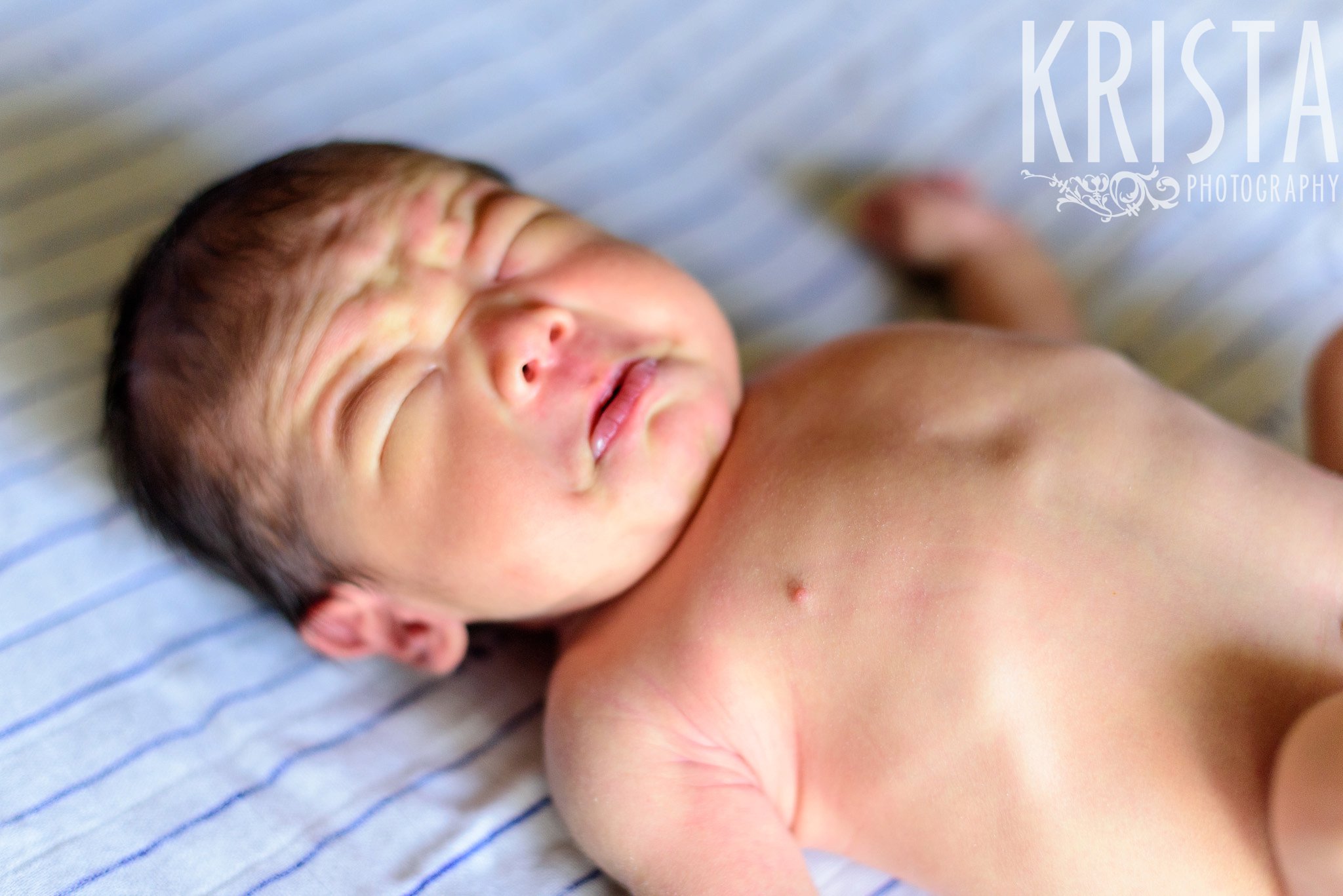 newborn baby boy with face scrunched up in tears during family portrait session at home