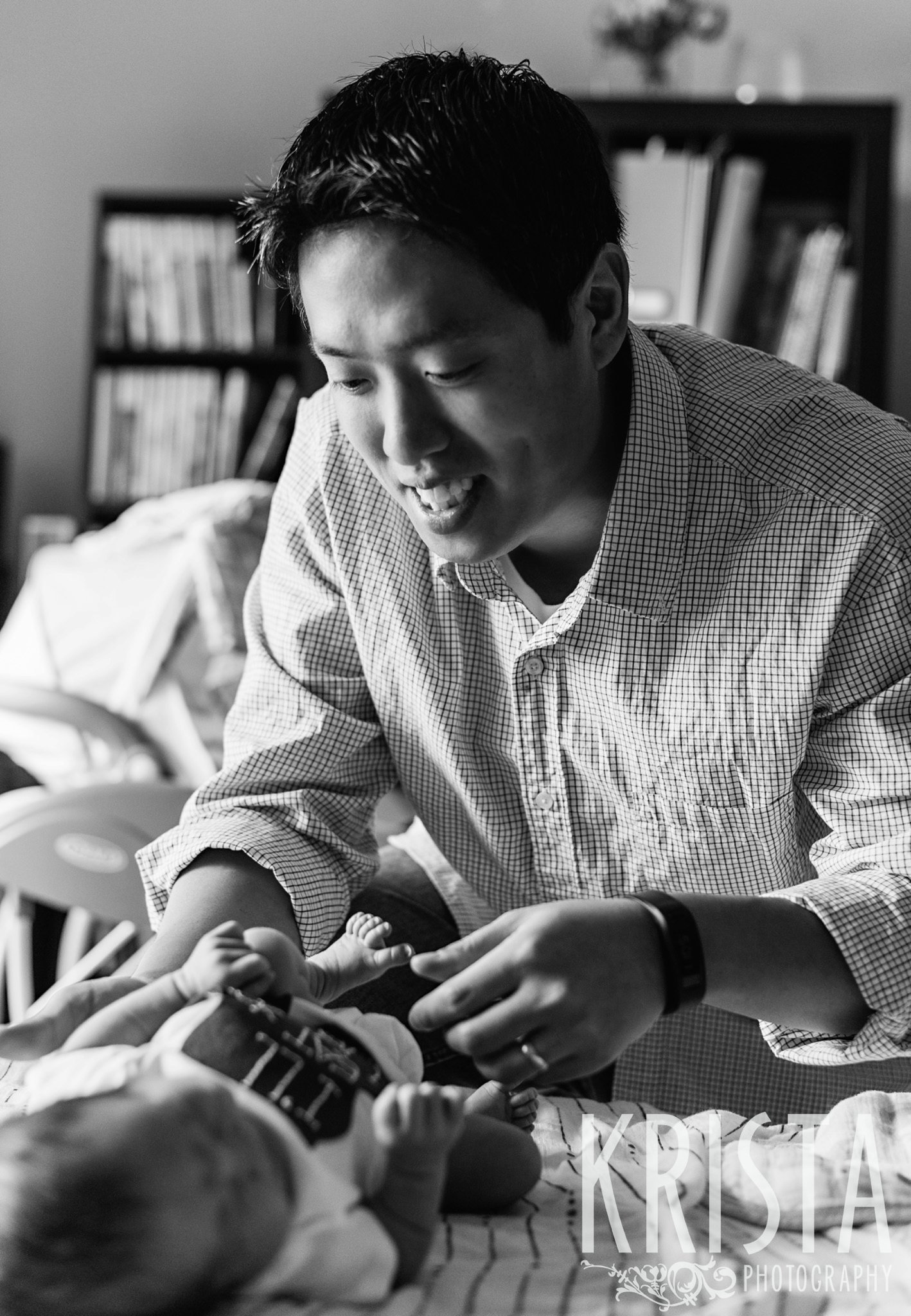 black and white image of father trying to cheer up newborn baby boy during portrait session at family home