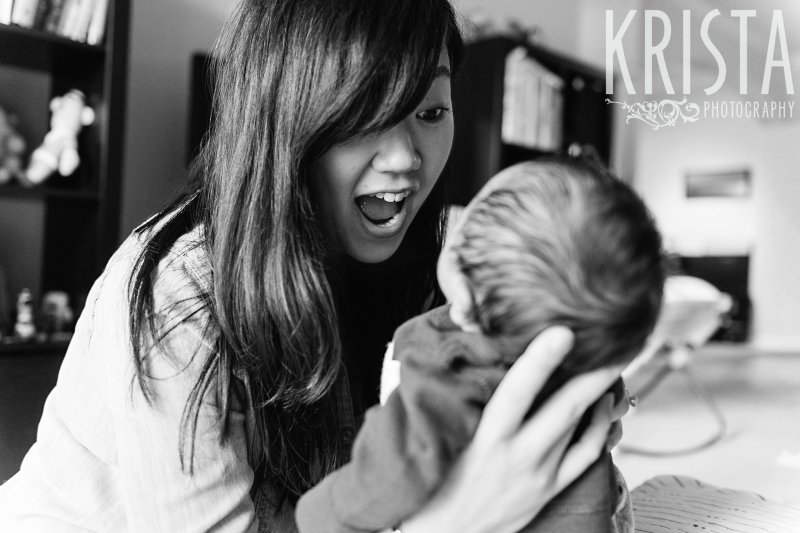 black and white image of mother trying to cheer up newborn baby boy during portrait session at family home