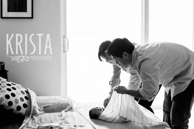 black and white image of parents swaddling newborn baby boy during portrait session at family's home