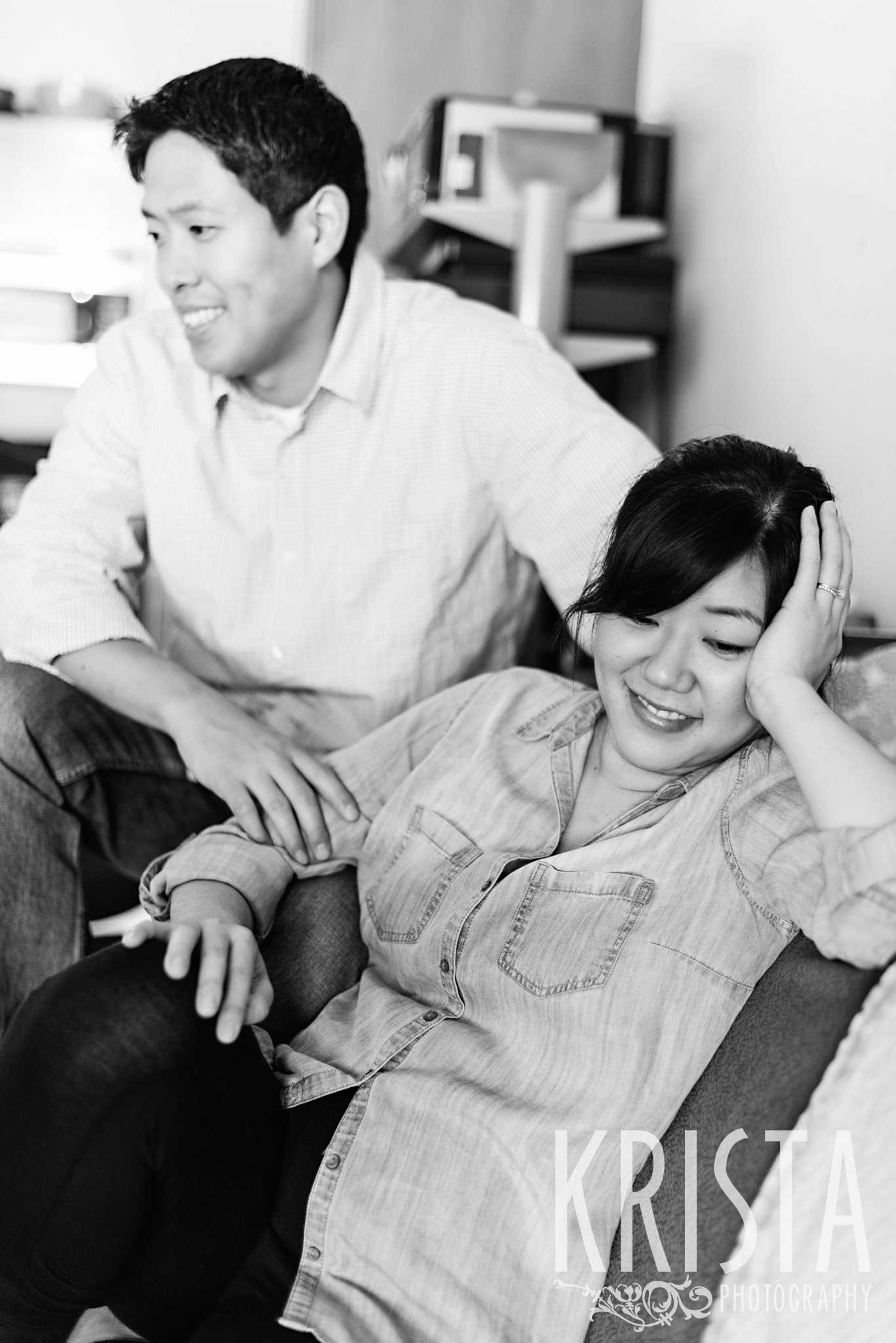 black and white image of tired new parents looking on as their newborn baby boy is photographed during family portrait session in their home