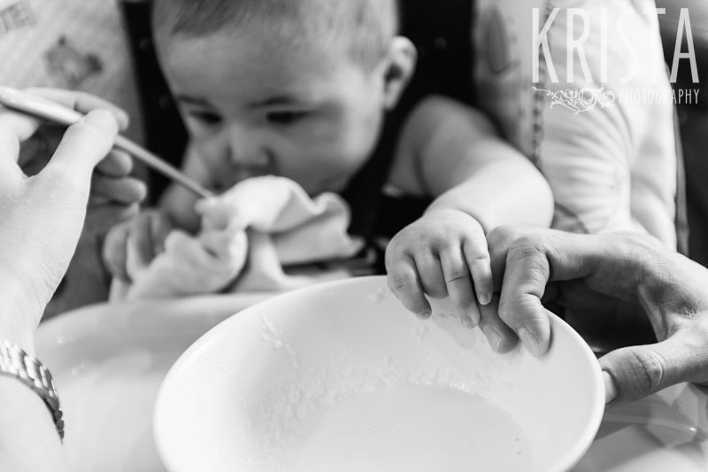 black and white image of baby trying first spoonfuls of cereal from parents and grandparents during lifestyle portrait session at home