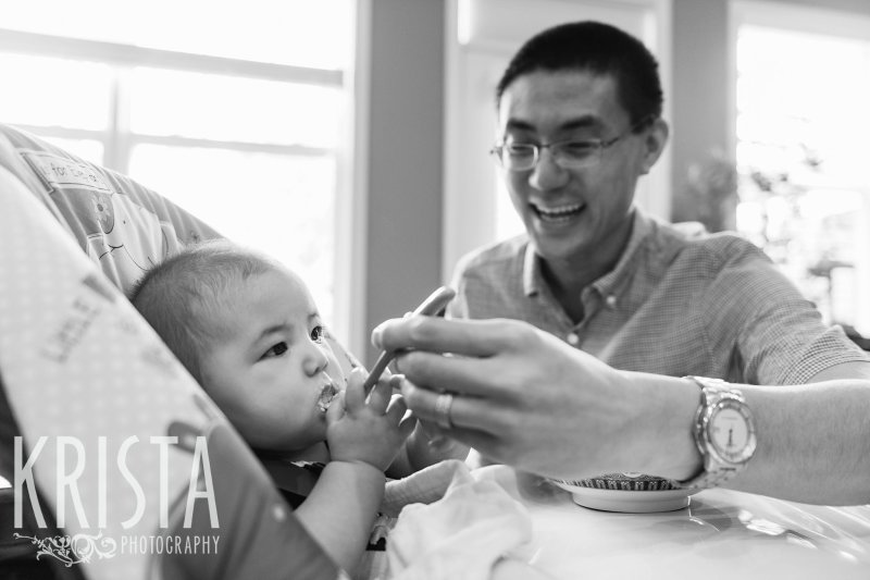 black and white image of baby trying first spoonfuls of cereal from parents and grandparents during lifestyle portrait session at home