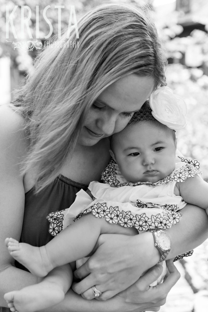 black and white image of mother with baby girl snuggling outside of home during lifestyle portrait session at home