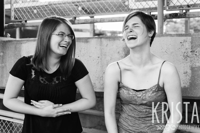 black and white image of sisters laughing during lifestyle portrait session near family's home
