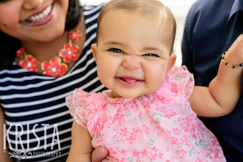 adorable smiley baby girl in parents' laps during lifestyle portrait session at home