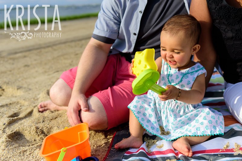 baby girl in turquoise patterned dress hitting beach shovels together on Cape Cod during lifestyle portrait session 