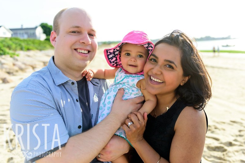 happy family with baby girl in aqua dress with bright pink sunhat on beach of Cape Cod during lifestyle portrait session