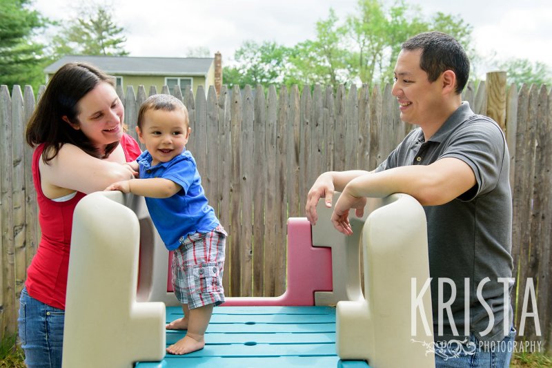 one year old baby boy standing on play slide in backyard during lifestyle portrait session at home