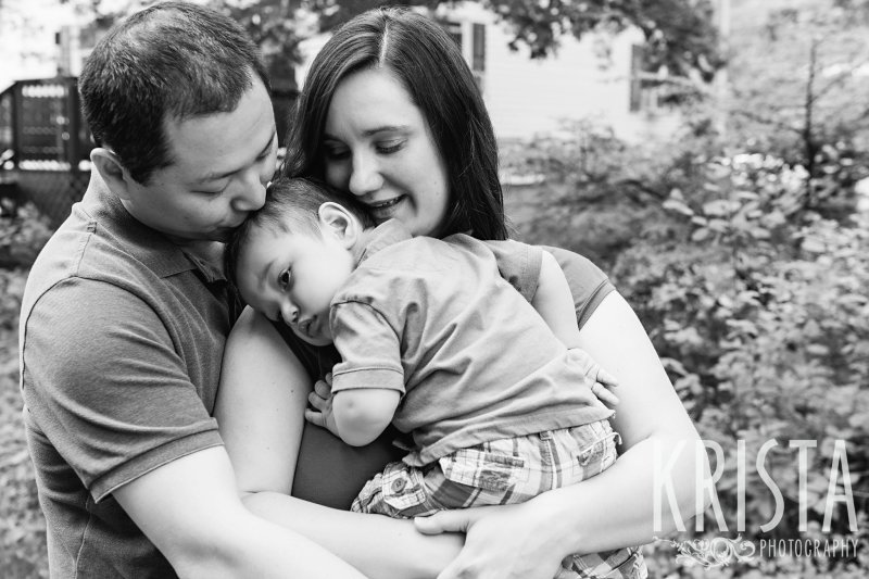 black and white image of parents with one year old son snuggling into mother during lifestyle portrait session at home