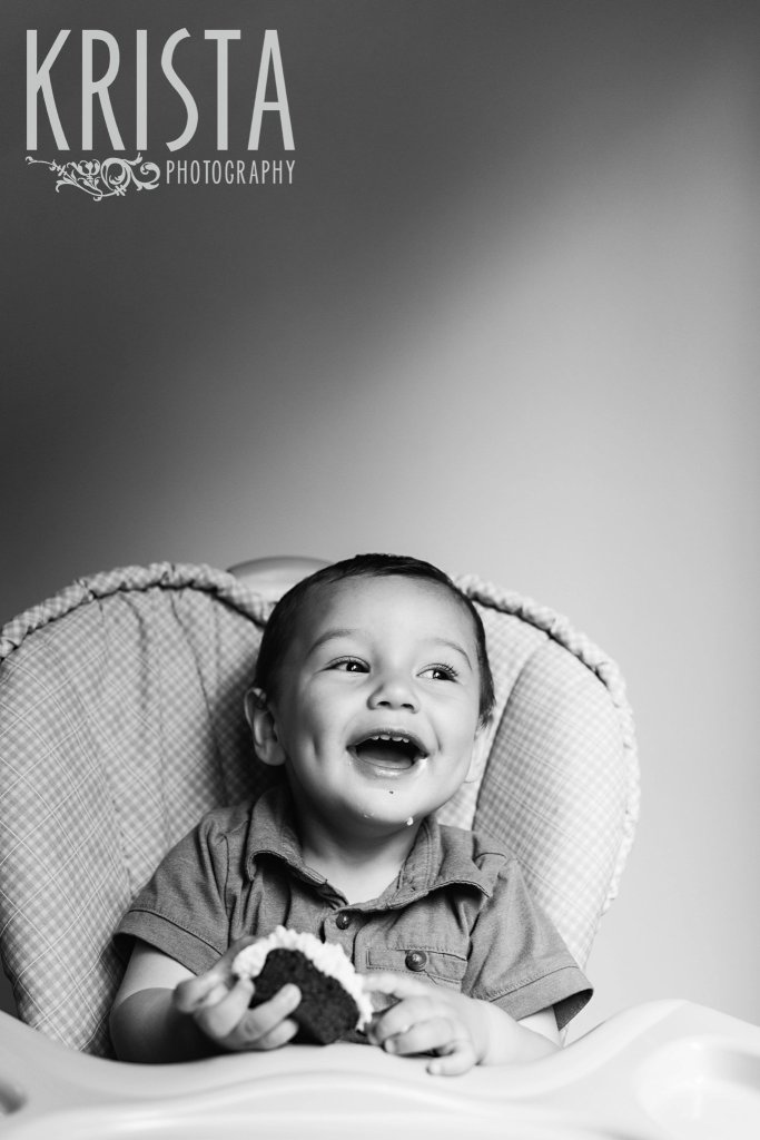 black and white image of one year old baby boy in highchair having first birthday cake during lifestyle portrait session