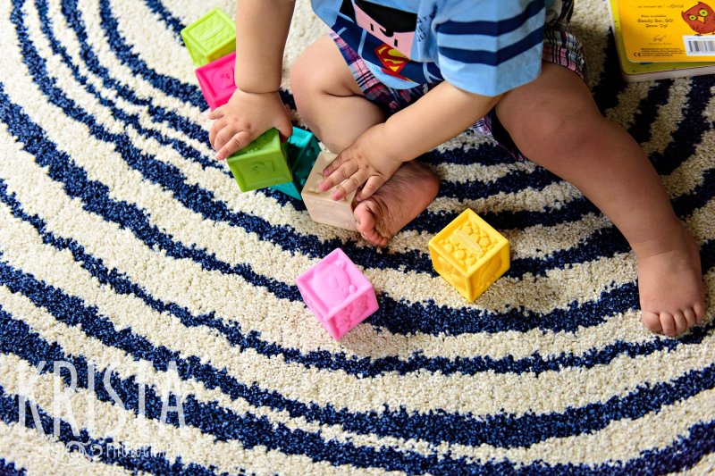 first birthday baby boy feet playing with blocks on white and blue carpet during lifestyle portrait session at home