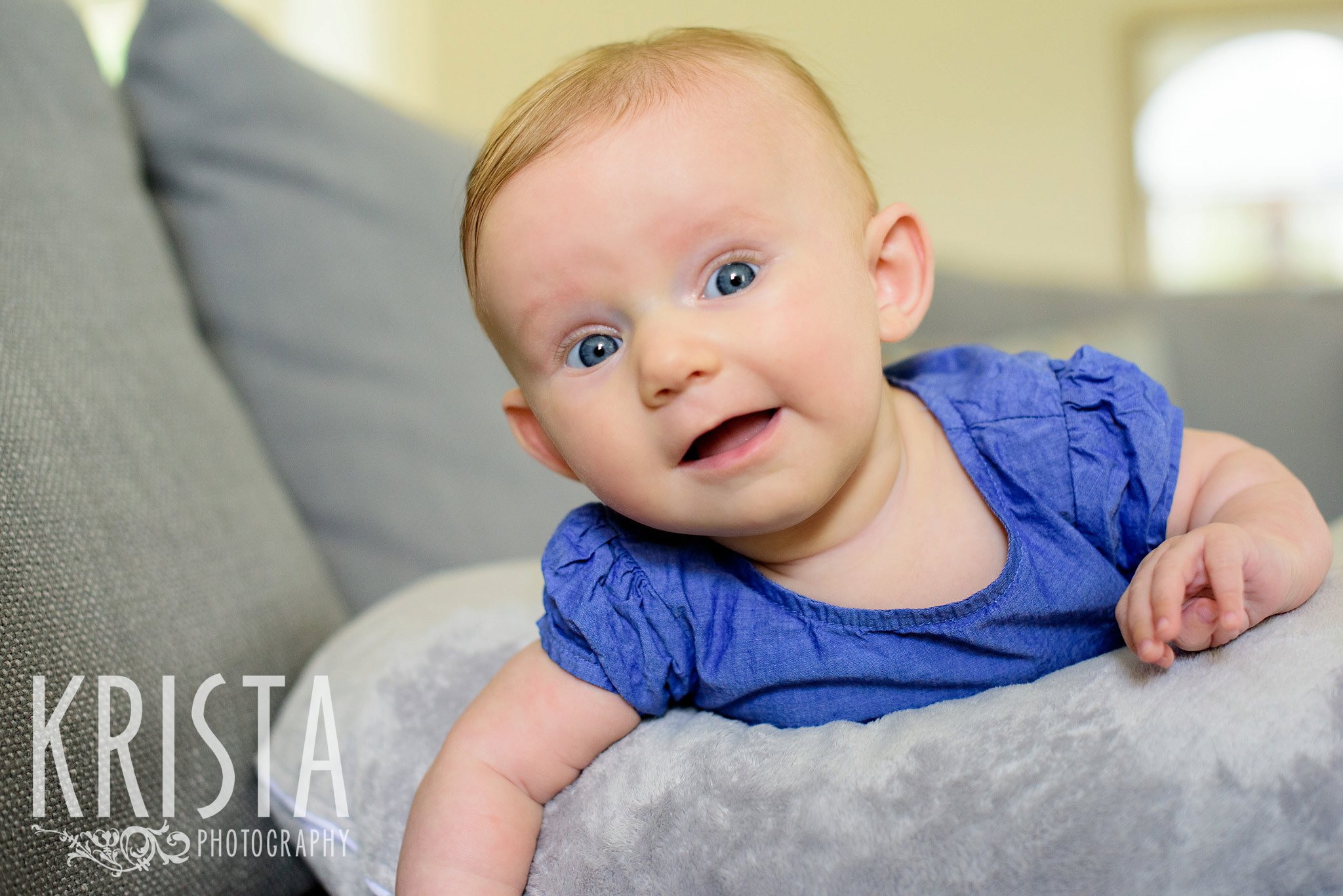 three month old baby girl laying on belly over pillow smiling on couch during lifestyle portrait session at family's home