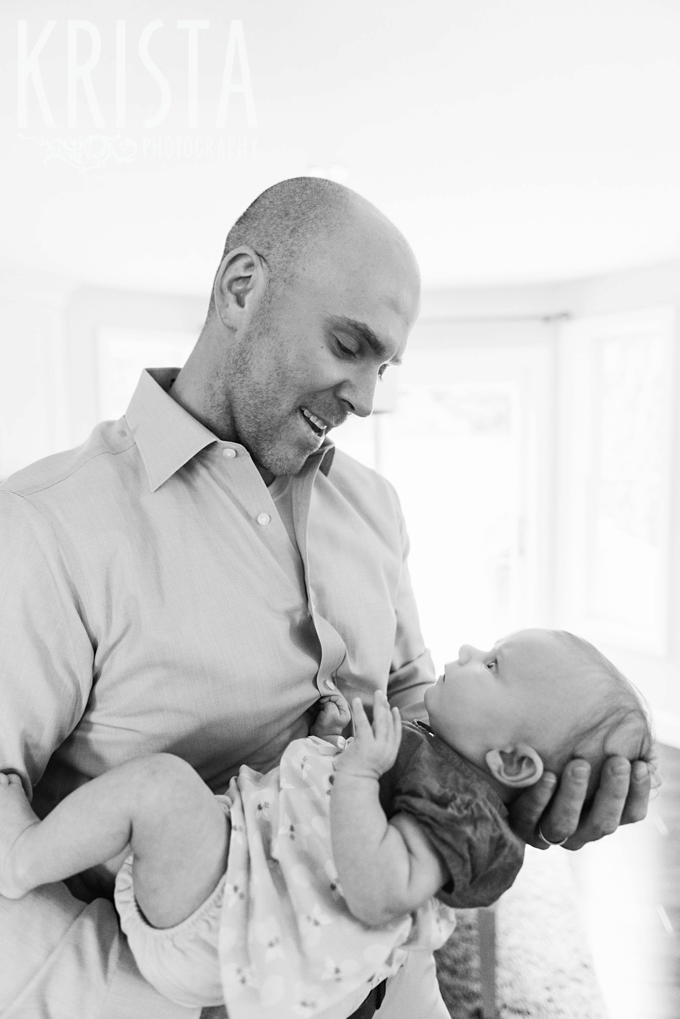 black and white image of father cradling three month old baby girl during lifestyle portrait session at family home