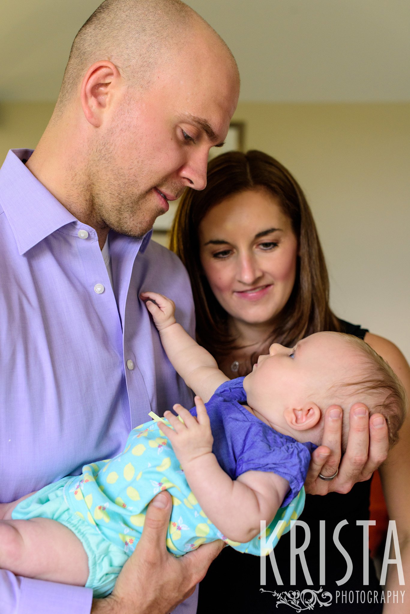 mom and dad holding three month old baby girl and looking at her during lifestyle portrait session at home