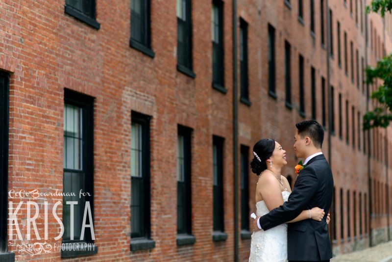 bride and groom snuggling in front of brick wall © Krista Photography