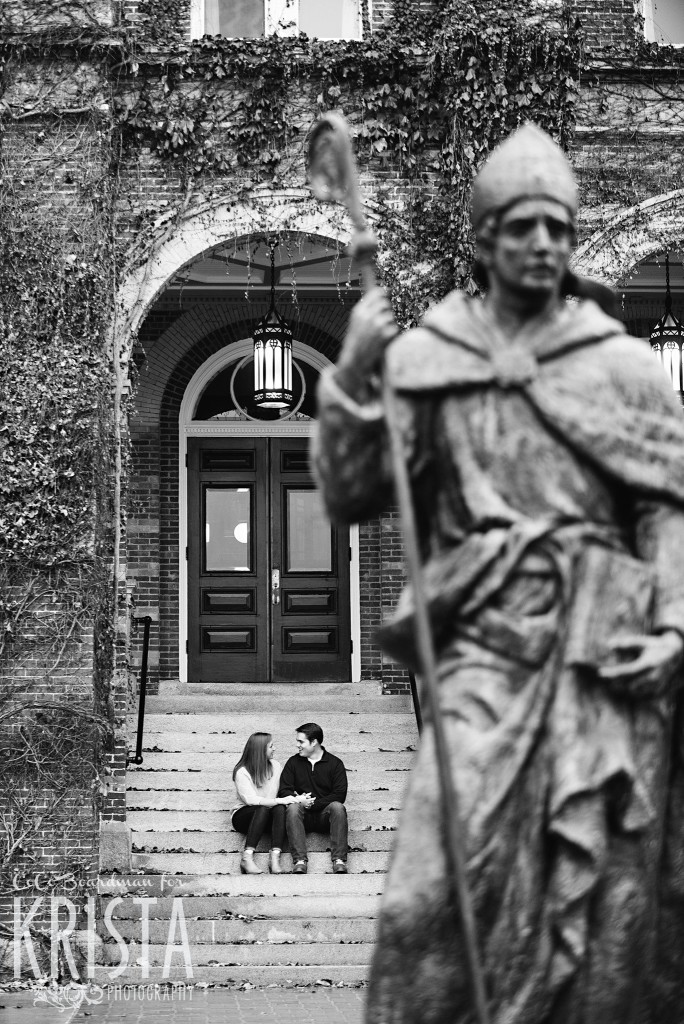 couple sitting on the steps behind statue at St. Anselm College - Saint Anselm Engagement